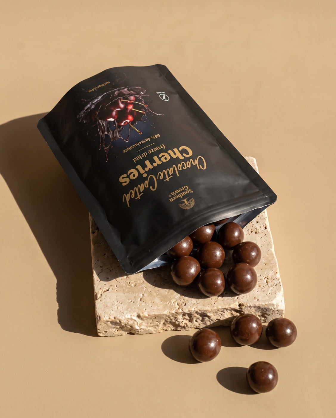 An open pack of Chocolate Coated Cherries spilling onto travertine.