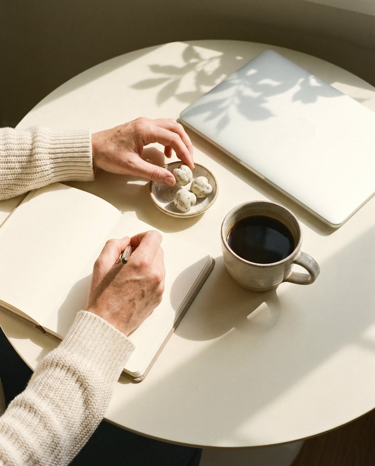 Yoghurt-coated cherries beside a notebook and coffee on a desk.