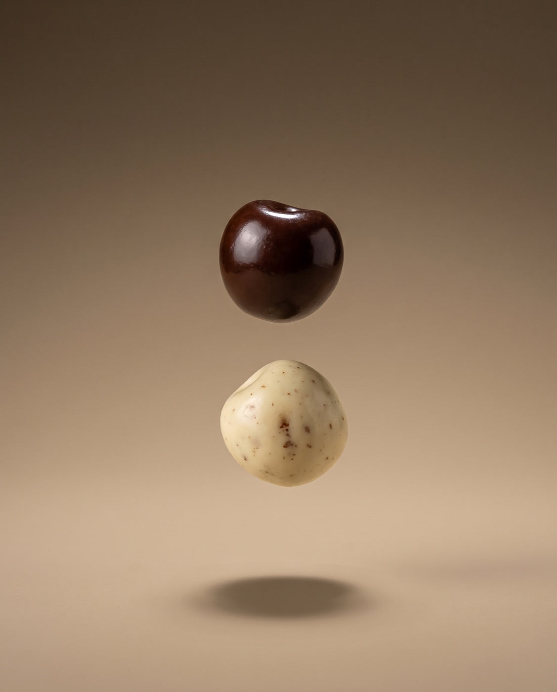 A chocolate-coated and a yoghurt-coated cherry suspended in warm light.
