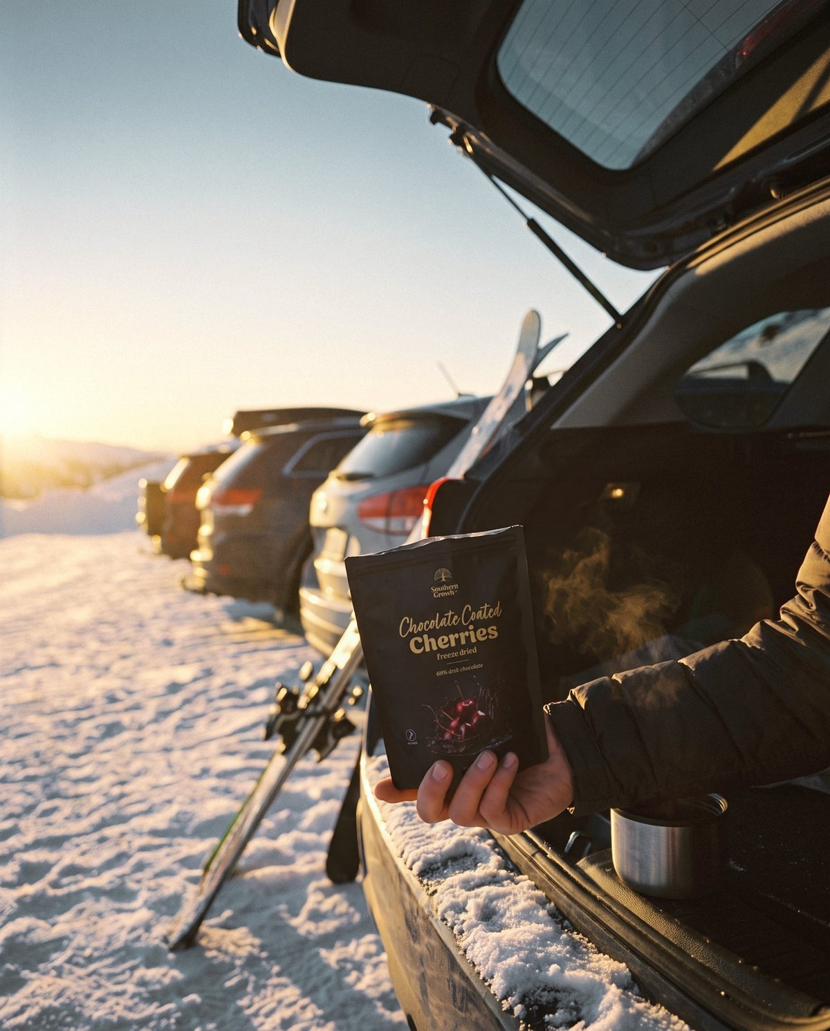 A pack of Chocolate Coated Cherries held at the open boot of a car in the snow.